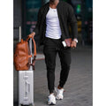 Man wearing a black zip jacket and jogger tracksuit with a suitcase